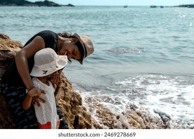 In this tranquil scene, an mother and child share a moment of coastal exploration. Standing on the rocky beach, they gaze out at the waves crashing against the shore - Powered by Shutterstock