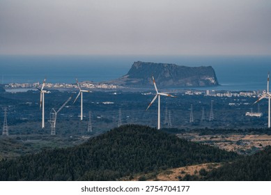 This unique panoramic view features Seongsan Ilchulbong (Sunrise Peak), a UNESCO World Natural Heritage site, rising majestically above the blue ocean alongside a modern wind farm. The contrast between the ancient volcanic landmark and the sleek white wind turbines creates a striking harmony of nature and sustainable energy, capturing the dynamic essence of Jeju Island.