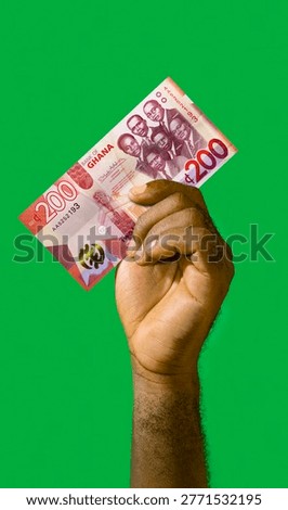 This vertical studio shot features a single African hand raised against a solid, vibrant green background. The hand, with a dark skin tone and visible forearm hair, firmly grips a 200 Ghanaian Cedi banknote. The bill is held at a diagonal angle, showcasing the 
