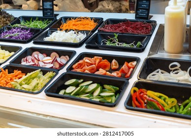 This vibrant display features a variety of fresh vegetables including leafy greens, shredded carrots, beets, radishes, cucumbers, tomatoes, peppers, and onions, arranged in black trays at a salad bar.