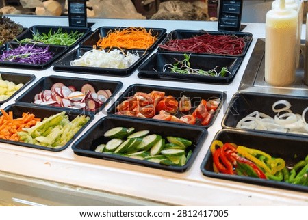 This vibrant display features a variety of fresh vegetables including leafy greens, shredded carrots, beets, radishes, cucumbers, tomatoes, peppers, and onions, arranged in black trays at a salad bar.