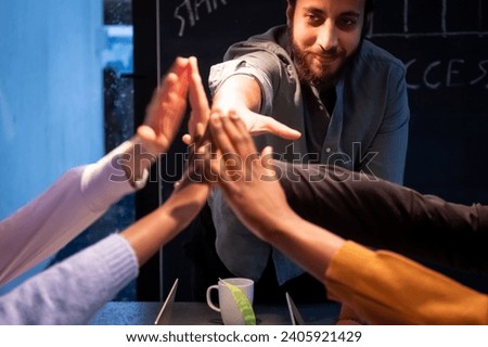This vibrant and dynamic image captures a moment of celebration and teamwork. A group of individuals, illuminated by warm, intimate lighting, is seen engaging in a high-five, symbolizing success and