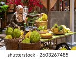 This vibrant image captures an authentic Southeast Asian street market scene, featuring a smiling woman in a floral hijab selecting a durian from a traditional fruit cart. 