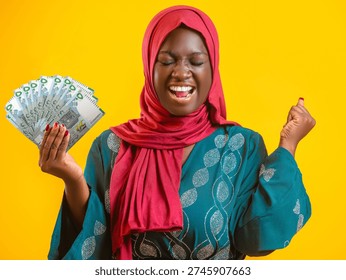 This vibrant image features a joyous woman of African descent wearing a red hijab and a teal patterned dress against a bright yellow background. She is celebrating enthusiastically, with her eyes closed and mouth open in a shout of triumph, one fist clenched in the air. In her other hand, she fans out a stack of Mauritanian Ouguiya banknotes. The high-contrast colors and her exuberant expression convey a powerful sense of financial success, winning, or newfound prosperity.