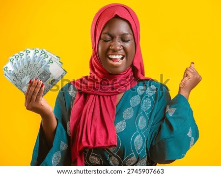 This vibrant image features a joyous woman of African descent wearing a red hijab and a teal patterned dress against a bright yellow background. She is celebrating enthusiastically, with her eyes closed and mouth open in a shout of triumph, one fist clenched in the air. In her other hand, she fans out a stack of Mauritanian Ouguiya banknotes. The high-contrast colors and her exuberant expression convey a powerful sense of financial success, winning, or newfound prosperity.