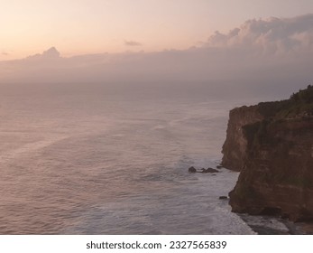 This is a view during sunset near a cliff at Uluwatu Temple, Bali, Indonesia. Uluwatu is known for white sand, amazing clifftop views, relaxing wave sounds and epic surfing quality - Powered by Shutterstock