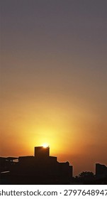 This is a view of sunset, particularly showing the humor that the sun is hiding behind the house. with a small plant above the house top make it look more special and nostalgia.