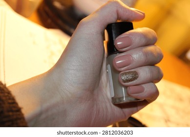 This visually appealing image portrays a well-groomed hand holding a bottle of nail polish, featuring a beautiful blend of neutral and glittering colors. The focus on the nails and polish bottle highlights the importance of personal care and creativity in beauty routines.