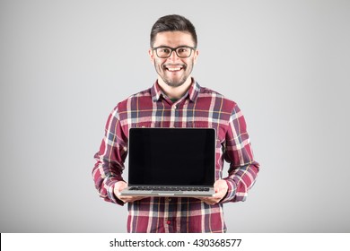 This Is What You Need! Confident Young Man Carrying Laptop And Showing Screen Of It Standing Against Gray Background