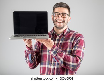 This Is What You Need! Confident Young Man Carrying Laptop And Showing Screen Of It Standing Against Gray Background