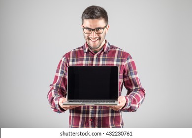 This Is What You Need! Confident Young Man Carrying Laptop And Showing Screen Of It Standing Against Gray Background