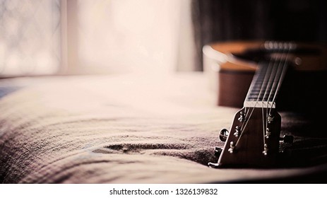 This is wooden basic classical guitar on bed. beautiful colouring blurry background effect.