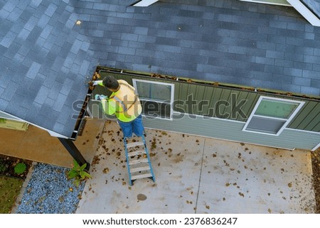 This worker is cleaning out clogged roof gutter drains that have become clogged with dirt, debris, fallen leaves
