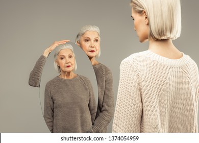 This is you. Nice aged woman holding an oval mirror while standing in front of herself young