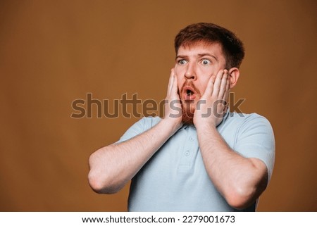This young redhead guy looks shocked and amazed while posing for the camera in a studio.