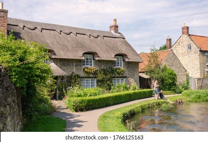 Thornton Dale, UK.  June 26, 2020.  Stone-built Picturesque Thatched Cottage In Thornton-le-Dale, North Yorkshire.  A Couple And Their Dog Enjoy The Cool Steam Beside The Building.