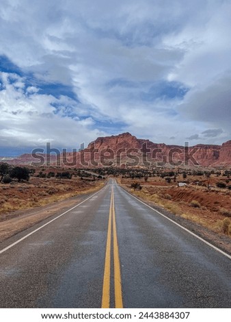 A thoroughfare cuts through a desert plain with mountains in the background, under a vast blue sky dotted with fluffy white clouds