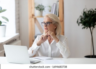 Thoughtful 60 years old businesswoman using laptop, pondering online project or startup ideas. Employee thinking about business vision sitting at office desk, manager solving business problem. - Powered by Shutterstock