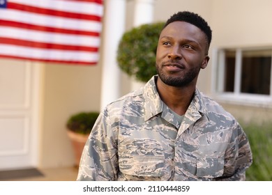 Thoughtful African American Army Man Looking Away Against House With America Flag. Patriotism And Identity, Unaltered.