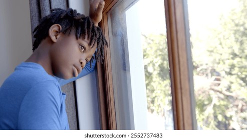 Thoughtful african american boy looking through window at home, slow motion. Childhood and domestic life, unaltered. - Powered by Shutterstock