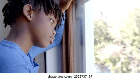 Thoughtful african american boy looking through window at home, slow motion. Childhood and domestic life, unaltered. - Powered by Shutterstock