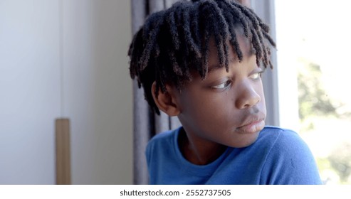 Thoughtful african american boy looking through window at home, slow motion. Childhood and domestic life, unaltered. - Powered by Shutterstock