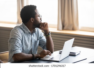 Thoughtful african American male employee in glasses sit at desk distracted from computer work pondering, pensive biracial man look in distance thinking or planning, business vision concept