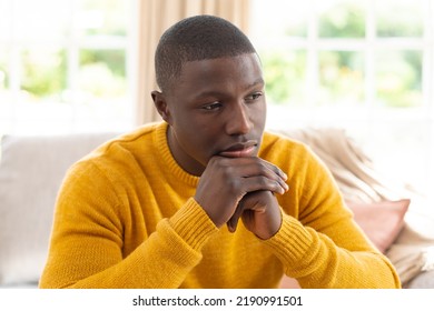 Thoughtful African American Man Sitting Couch At Home Looking Away, Resting Chin On Clasped Hands. Inclusivity, Domestic Life, Spending Time Alone At Home.