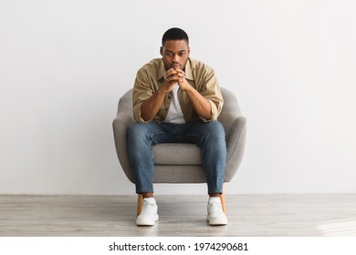 Thoughtful African American Man Thinking Sitting In Chair Over Gray Wall Background Indoors. Full-Length Shot Of Pensive Millennial Guy Reflecting On Problems, Front View - Powered by Shutterstock