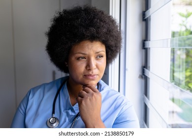 Thoughtful african american mid adult female nurse with hand on chin looking through window. unaltered, healthcare worker, contemplation, expertise and occupation concept. - Powered by Shutterstock