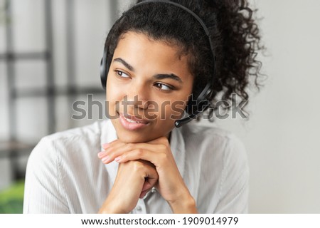 Thoughtful African American millennial woman in a headset is listening to an online webinar, sitting with her hands on a chin, working in the customer service department as a call center operator