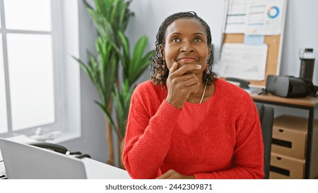 A thoughtful african american woman in a red sweater sits pensive in a bright office setting. - Powered by Shutterstock