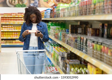 Thoughtful African American woman shopping at grocery store. Serious young customer standing with shopping cart and reading information on packaging. Shopping concept - Powered by Shutterstock