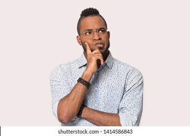 Thoughtful african guy thinking try solve problem pose isolated on grey studio background, worried black man in glasses feels concerned puzzled lost in thoughts pondering making decision concept image