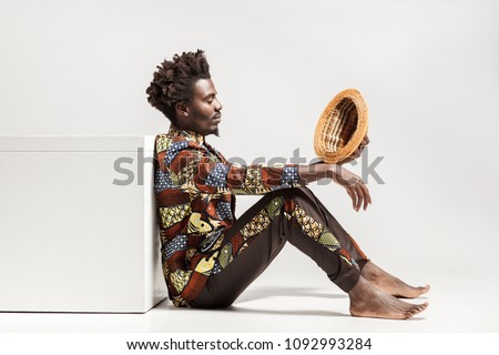 Thoughtful african man looking on hat and musing. Indoor, isolated on gray background