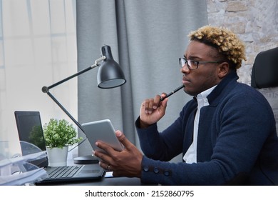 Thoughtful African Man Sitting At A Table By Window, Holding A Digital Tablet And Pen In His Hands, Thinking About Solving A Problem, Thoughtful Male Employee Thinking About An Idea, Making A Decision