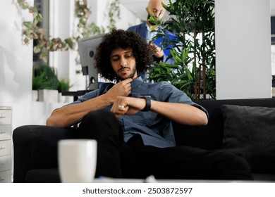 Thoughtful arab entrepreneur checking work schedule on smartwatch in business office. Pensive planning calendar using electronic watch to meet project deadline while sitting in coworking space - Powered by Shutterstock