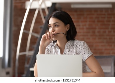 Thoughtful Asian businesswoman taking off glasses, pondering ideas, developing business strategy, looking in distance, using laptop, pensive employee taking break, dreaming or visualizing in office