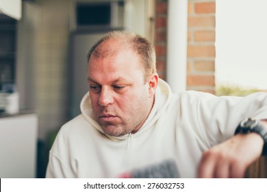 Thoughtful balding middle-aged man sitting indoors at home staring at the floor with a serious expression - Powered by Shutterstock