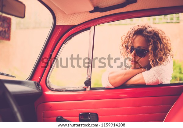 thoughtful  and\
beautiful caucasian middle age curly blonde woman smile and enjoy\
the outdoor leisure activity near her red vintage classic car.\
ready to travel and live the\
day
