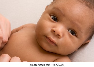Thoughtful biracial mix of Hispanic and African American infant lying down on yellowish colored blanket