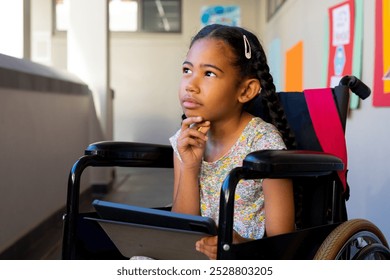 Thoughtful biracial schoolgirl sitting in wheelchair and using tablet at elementary school corridor. Technology, disability, education, childhood, development, learning and school, unaltered. - Powered by Shutterstock