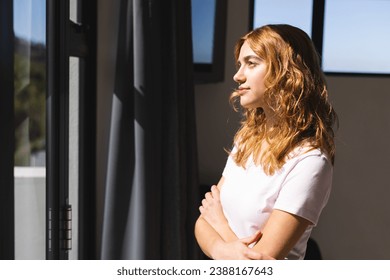 Thoughtful biracial woman looking through window at home, smiling on sunny day, copy space. Summer, lifestyle and domestic life, unaltered. - Powered by Shutterstock