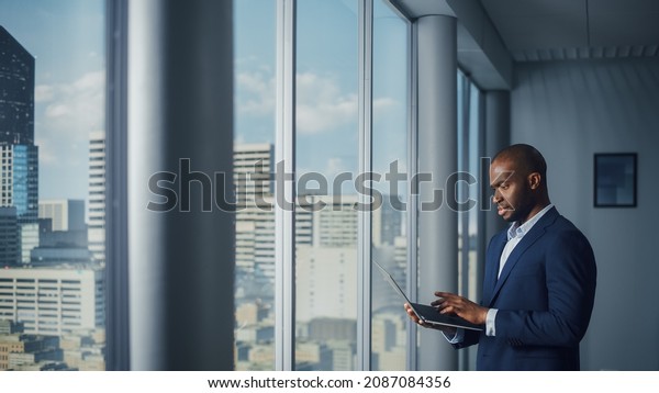 Thoughtful\
Black Businessman in a Tailored Suit Using Laptop while Standing in\
Office Near Window on Big City. Successful Corporate Top Manager\
Doing Data Analysis for e-Commerce\
Startup