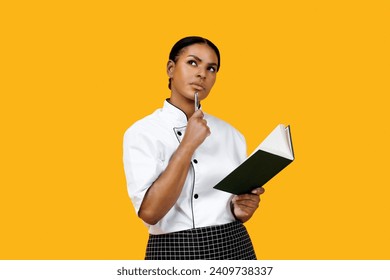 Thoughtful black female chef with notebook, deeply engrossed in crafting her culinary creations, pensive african american cook woman standing against bright yellow background, developing recipe - Powered by Shutterstock