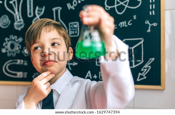 Thoughtful boy dressed as chemist with flask in\
front of a blackboard with\
drawings