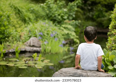 Thoughtful boy sitting by a pond in a calm, peaceful setting at Tupare Gardens in New Plymouth, North Island, New Zealand - Powered by Shutterstock