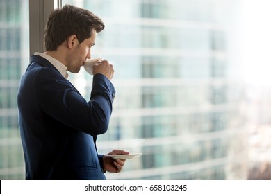 Thoughtful businessman drinking coffee, looking through window at big modern city, having break, deep in thoughts, enjoying view, waiting for meeting to start, making business decision, copy space - Powered by Shutterstock