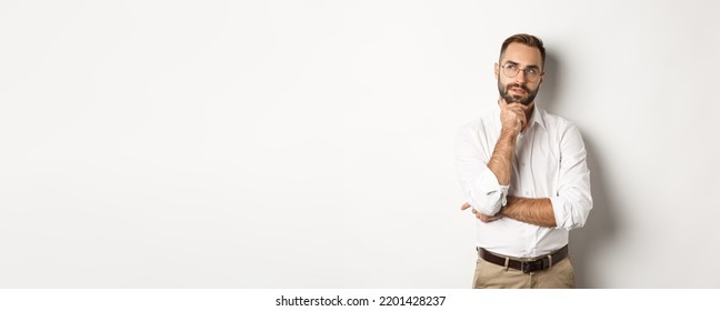 Thoughtful businessman in glasses making plan, looking at upper left corner and thinking, standing against white background
