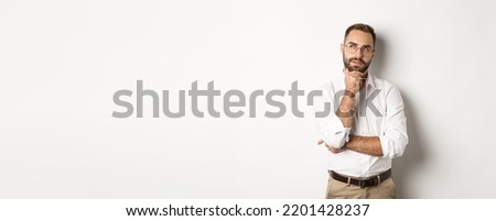 Thoughtful businessman in glasses making plan, looking at upper left corner and thinking, standing against white background